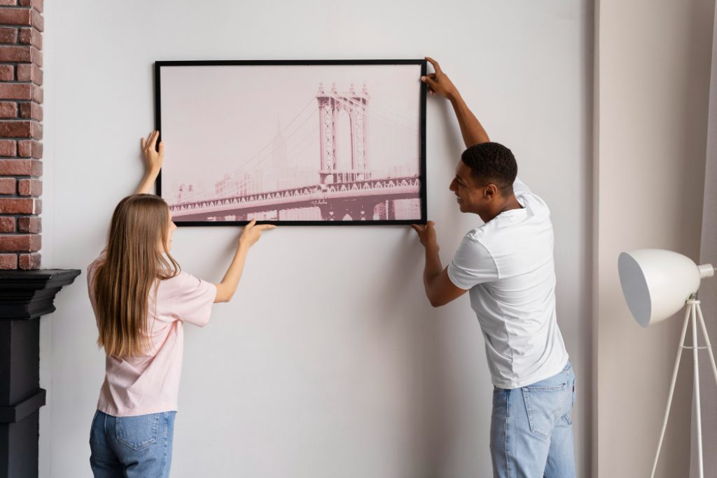 un couple accrochant un tableau au mur