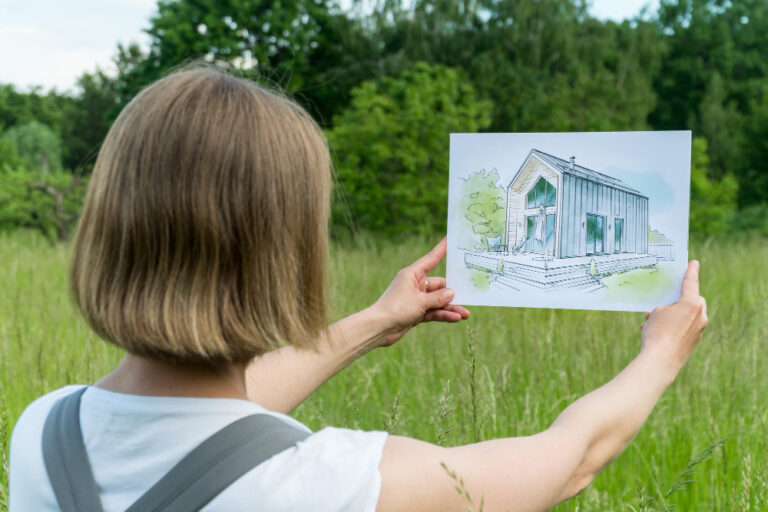 une femme tenant un plan de maison dans ses mains en regardant un terrain vide
